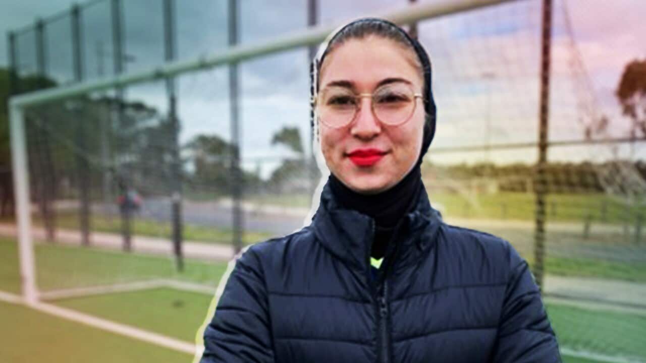 Mursal, wearing a black parka and glasses, standing outside in front of a football goal