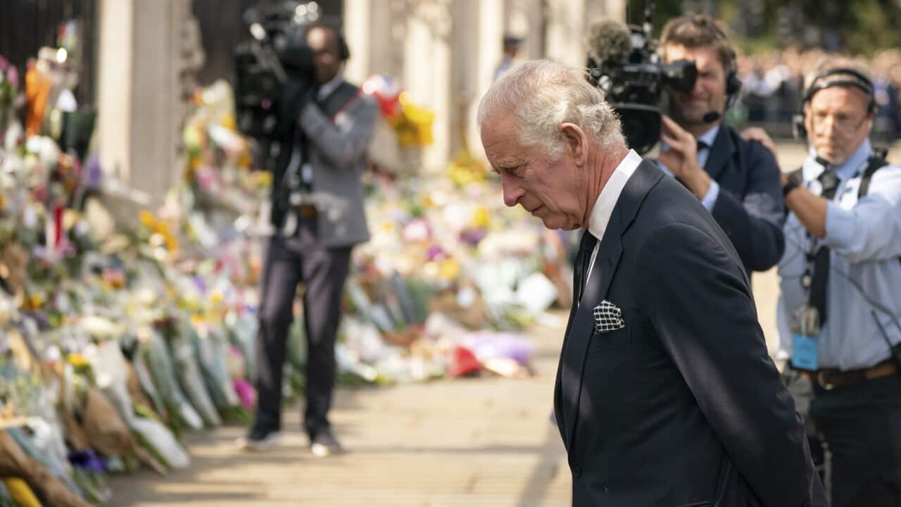 King Charles III looking at flowers and tributes.