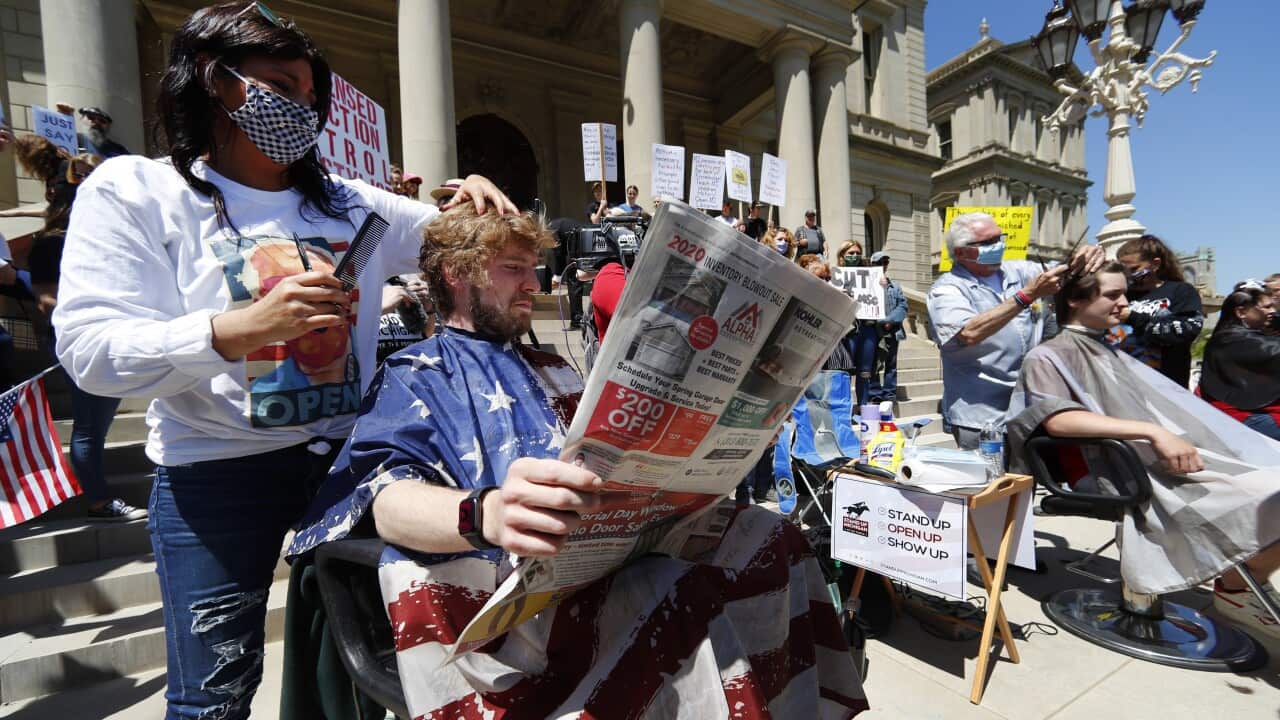 Jody Hebberd, left, gives a free haircut to Reid Scott, as he reads the paper on the steps of the State Capitol in Lansing, Michigan.