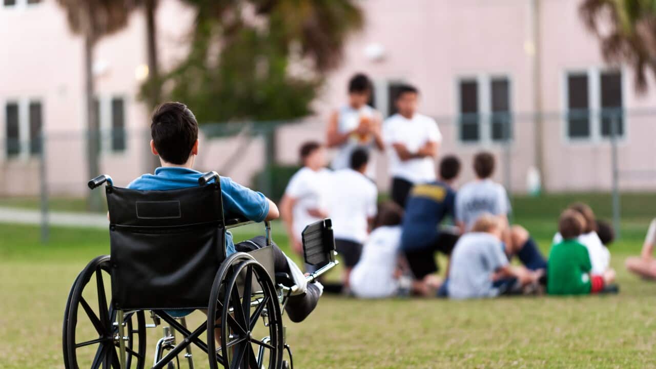 A young disabled boy looking upon his peers leaving him out