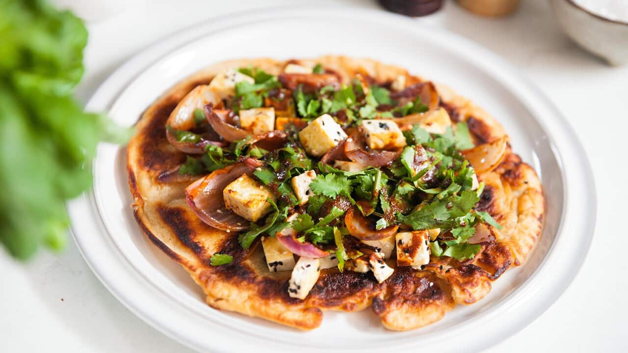 A round of bread is topped with tofu, cooked onion and fresh coriander.
