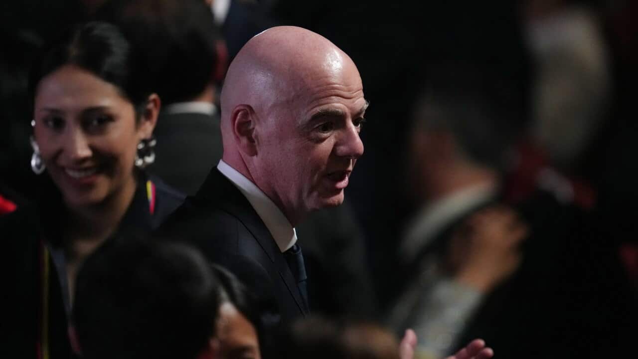 A bald man dressed in a dark suit in a crowd of people.