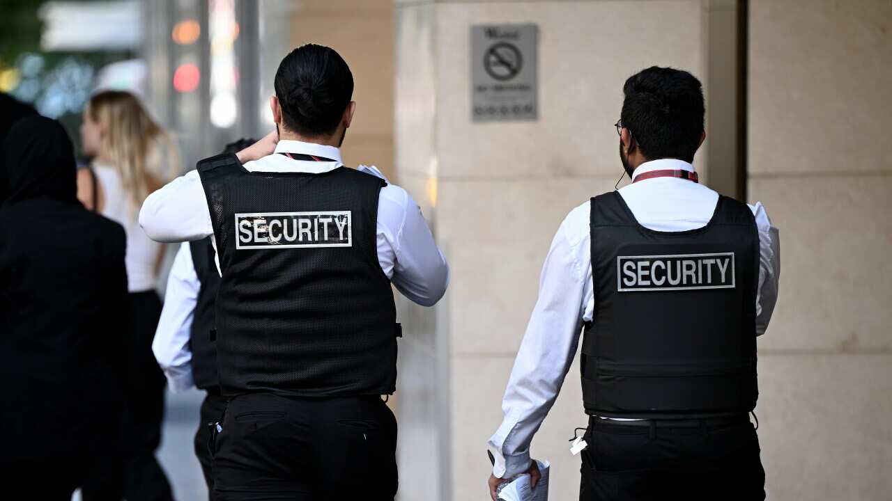 Rear view of two men wearing dark vests with Security written in capital letters across the back