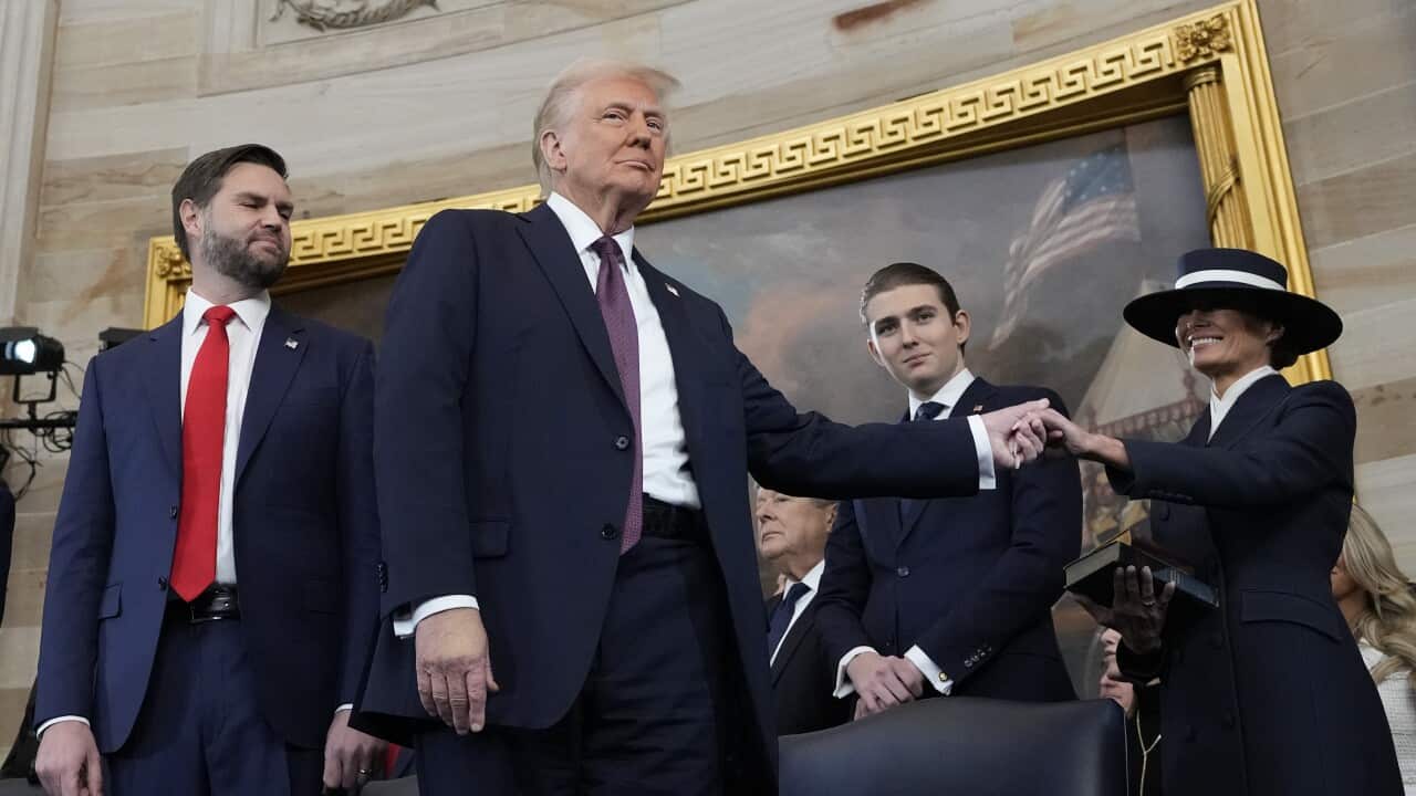 Man holding hand of woman in a wide brimmed hat, people looking on and smiling.