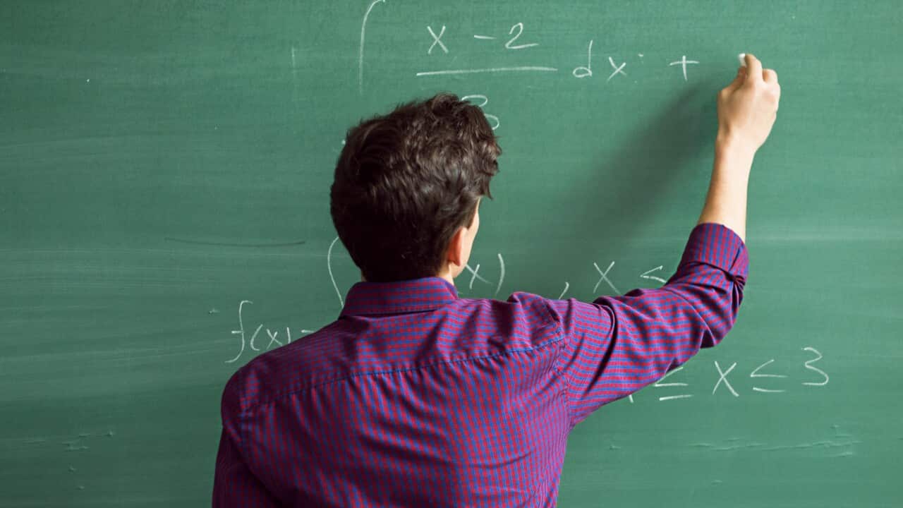 A man writing on a chalk board.