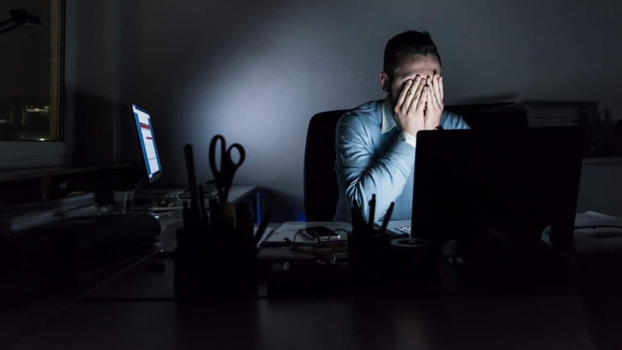 A stressed, exhausted businessman sitting at his desk in an office at night