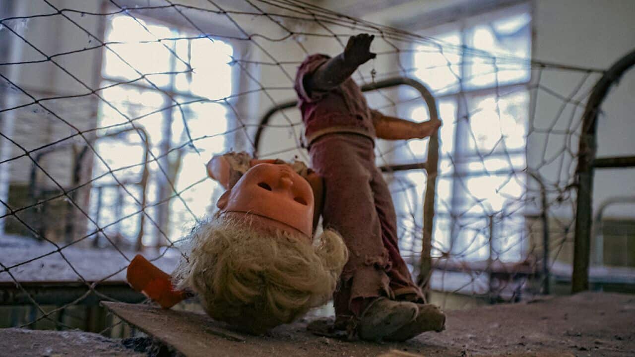 A broken doll lies on a bed in an abandoned room.