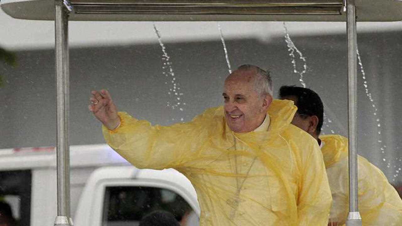 Wearing a yellow raincoat, Pope Francis waves to the faithful as he arrives in Tacloban, Philippines