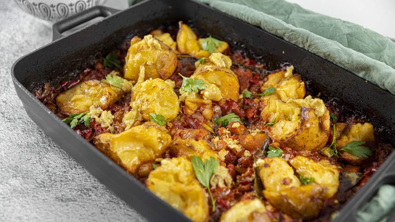 A rectangular cast-iron baking dish is filled with golden roast potatoes in a red sauce.
