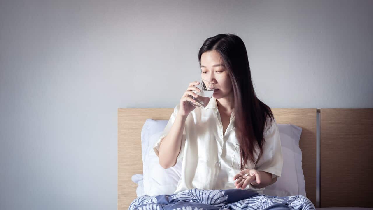 sick person taking a painkiller pill medicine in hand with a glass of water, sitting on cozy bed under blanket. sick at home