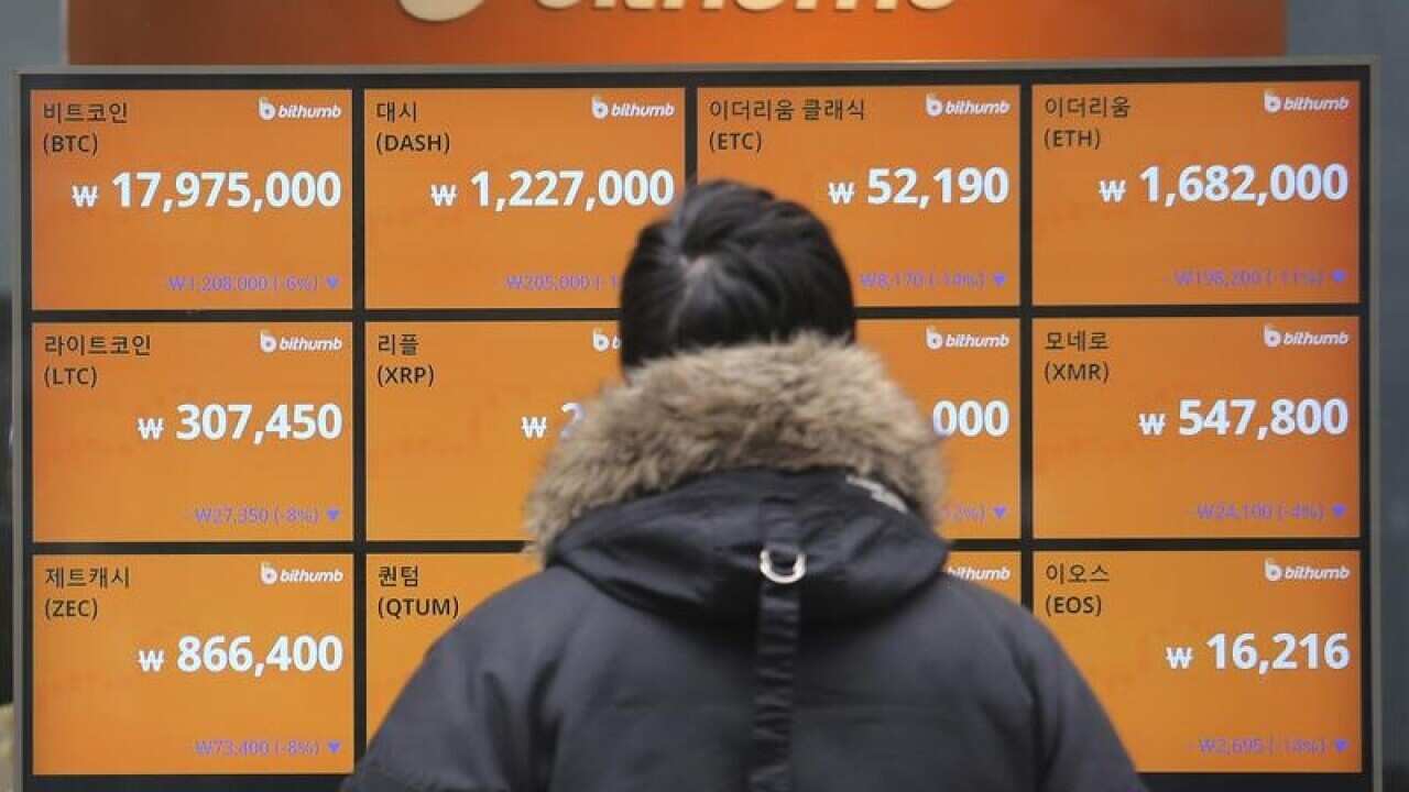 man viewed from behind, watches a noticeboard showing bitcoin's plunge