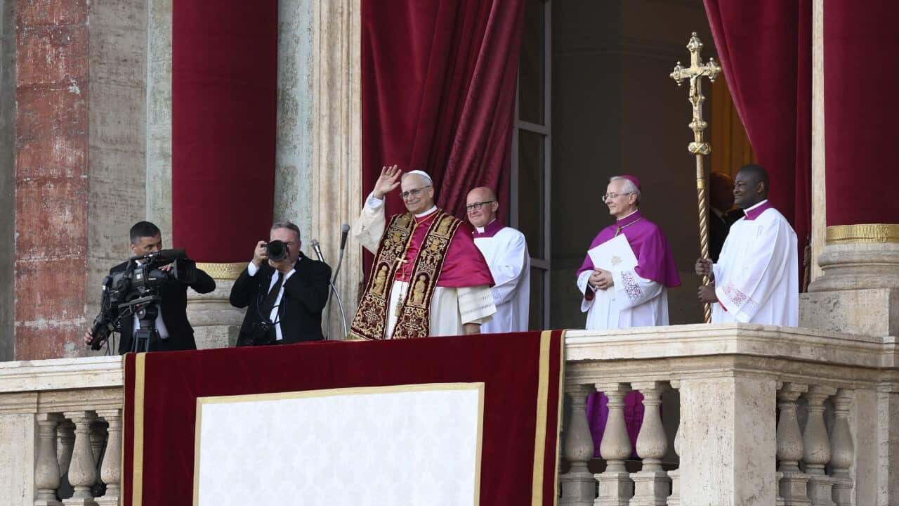 Cardinal Robert Francis Prevost, flanked by media photographers and clergymen, waves from the balcony of St Peter's Basilica.