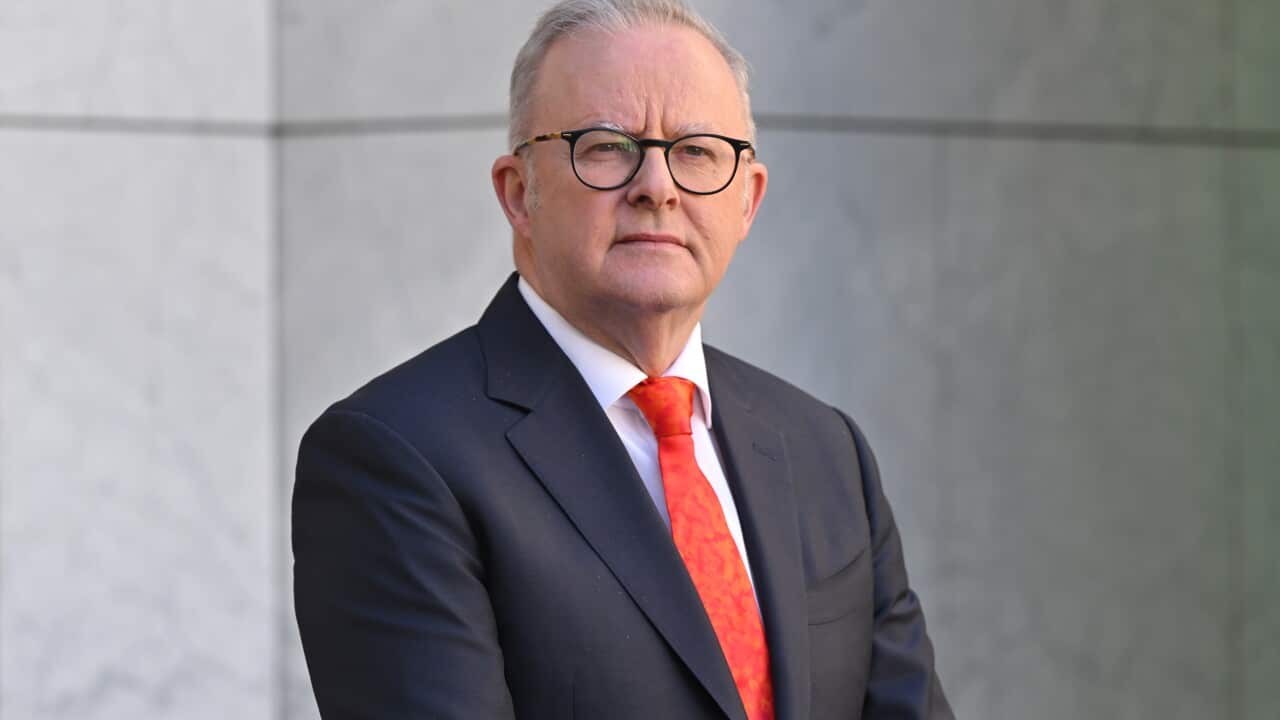 A middle-aged white man wearing a black suit and red tie