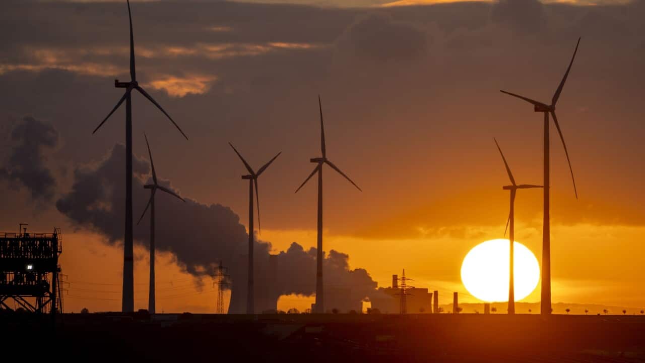Steam rises from a coal-fired power plant with wind turbines nearby.