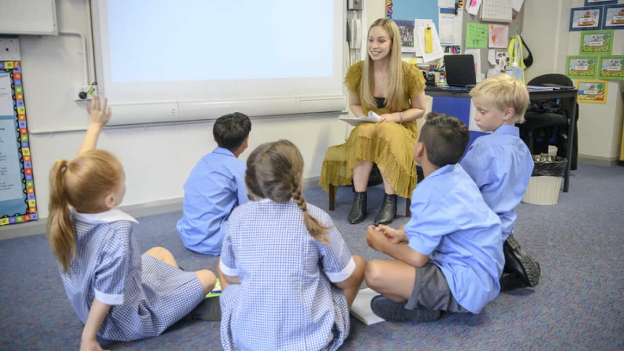 Group of school children sitting on the floor listening to their teacher
