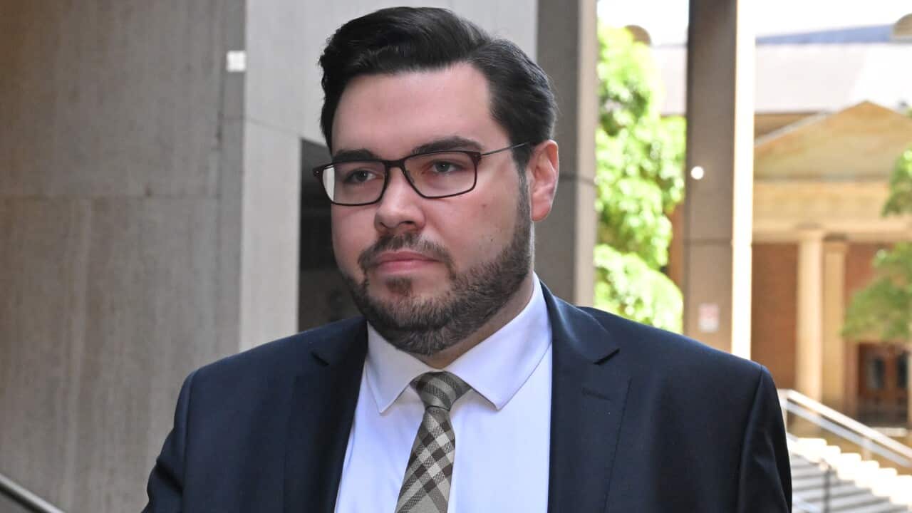 A man wearing a suit, tie and glasses who is walking outside.