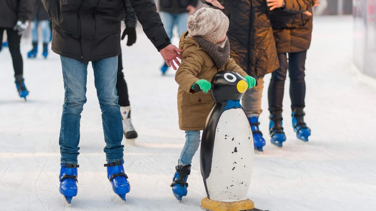 Children learning how to skate on the frozen surface of the an ice rink during a winter fair