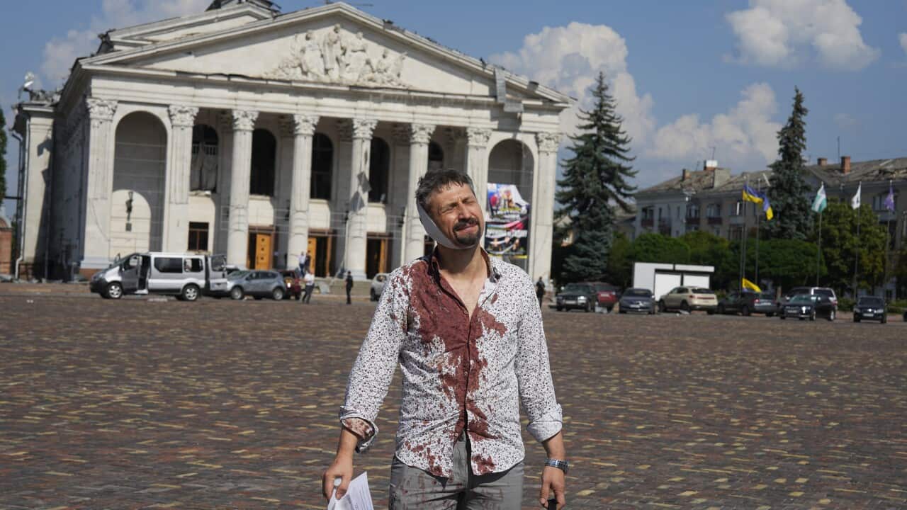An injured man with blood on his shirt walks in front of a building after a missile strike.