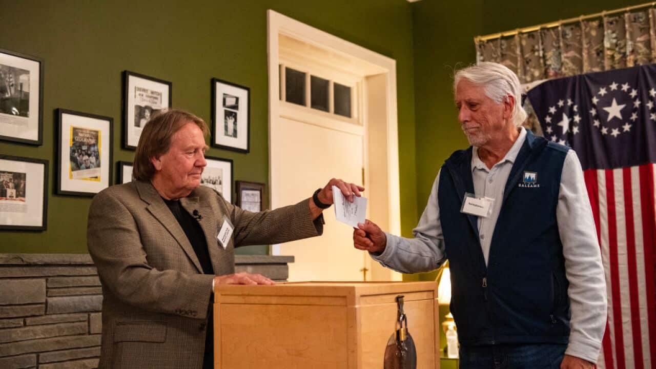 Two men holding a piece of paper over a wooden box in a room