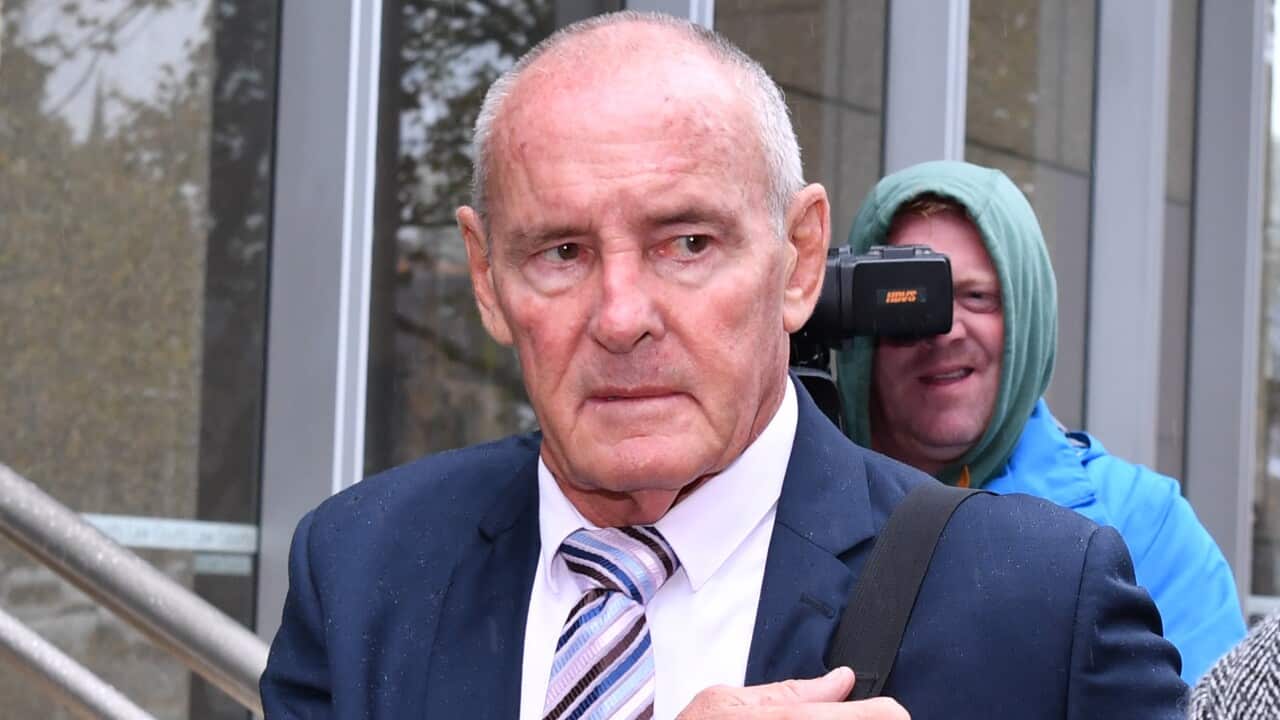 A man with short grey hair wearing a navy suit and tie looks to his left.