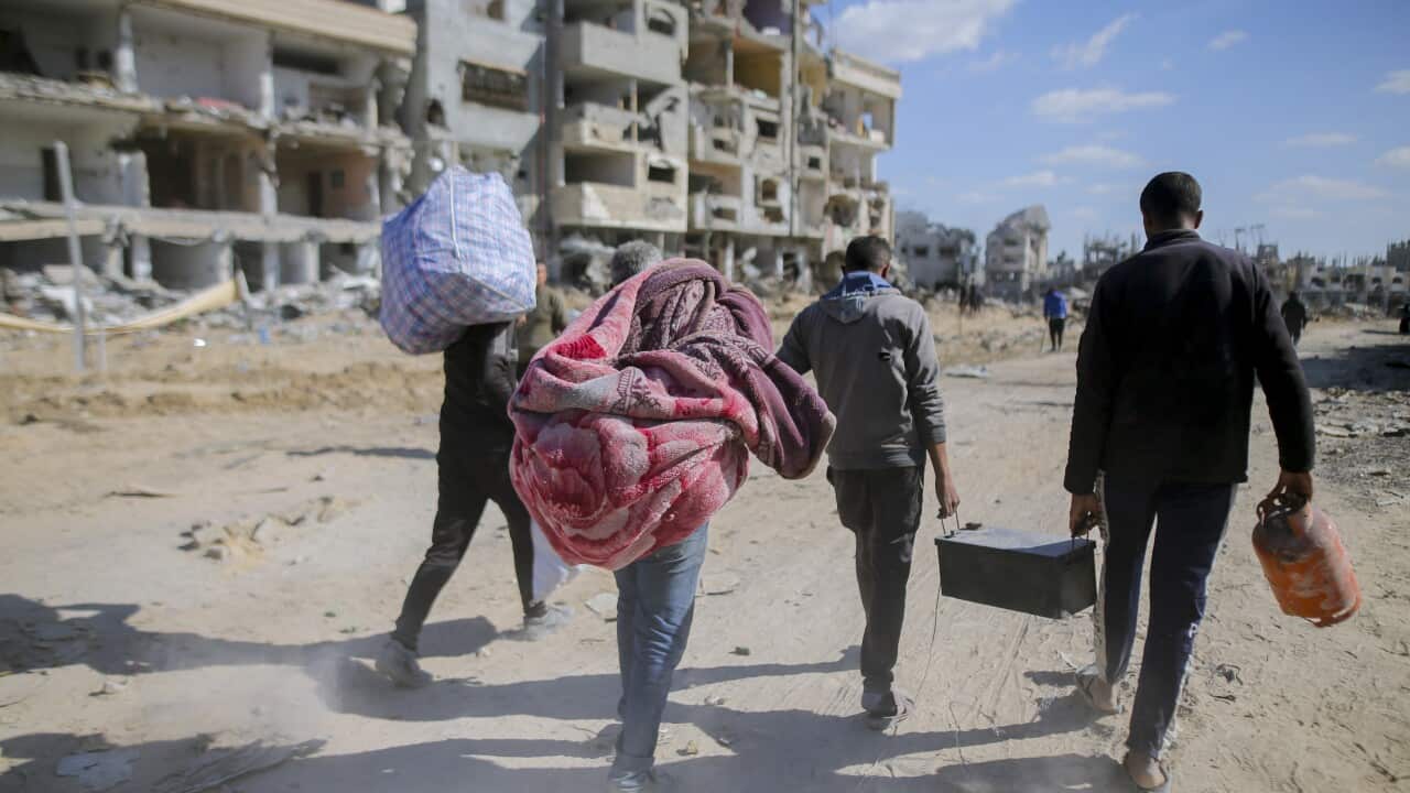 Rear view of four people with their belongings walking among ruins