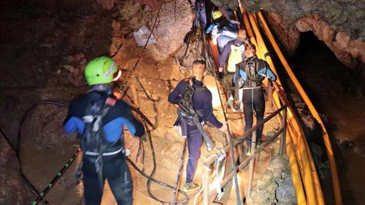 Thai rescue team members walk inside a cave where 12 boys and their soccer coach were trapped.