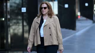 A woman in a camel coat and black sunglasses walks outside a court building