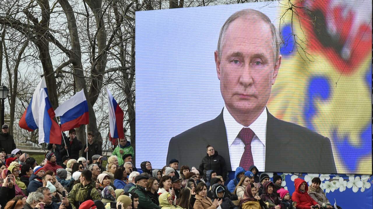 People sit under a screen with Russian President Vladimir Putin as they attend an event on the ninth anniversary of Russia's annexation of Crimea in Sevastopol, Crimea, 18 March 2023.