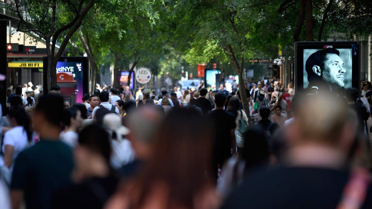A large crowd of people moving through an outdoor shopping centre.