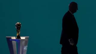 A shadowy bald man walks away from a gold trophy on a dais.