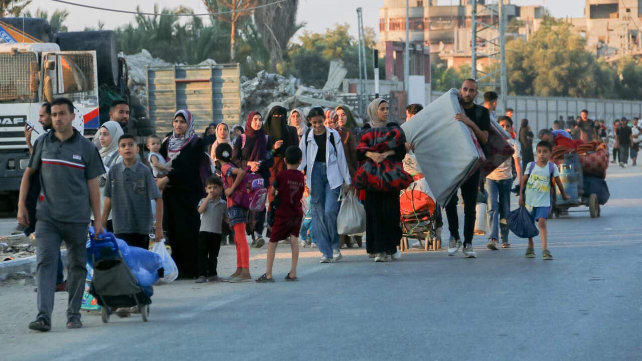 People walking with their belongings, including bags and mattresses over their shoulders.