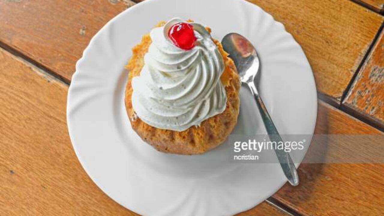 Savarin cake with cream and syrup, silver spoon, white plate on wood background.