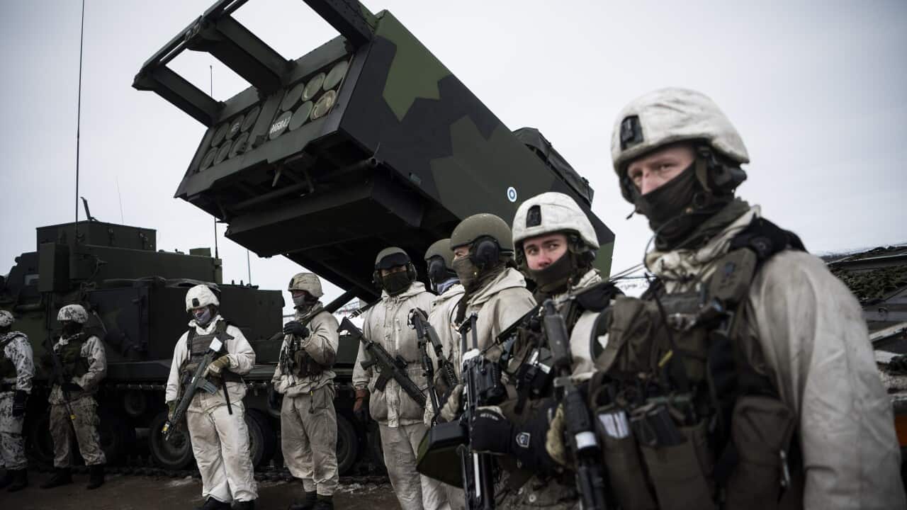 Swedish troops wearing white uniforms line up in front of a missile launcer