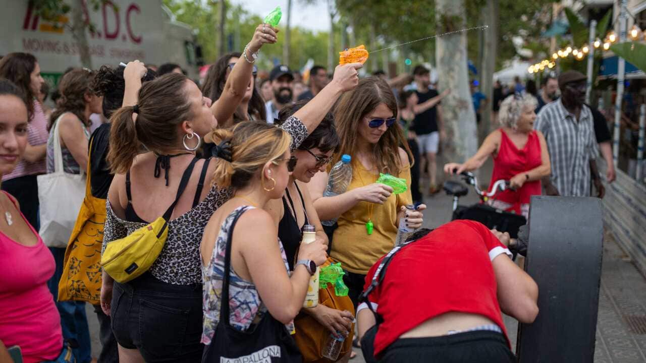 A crowd of people in colourful clothing holding water pistols, some of which are being fired.