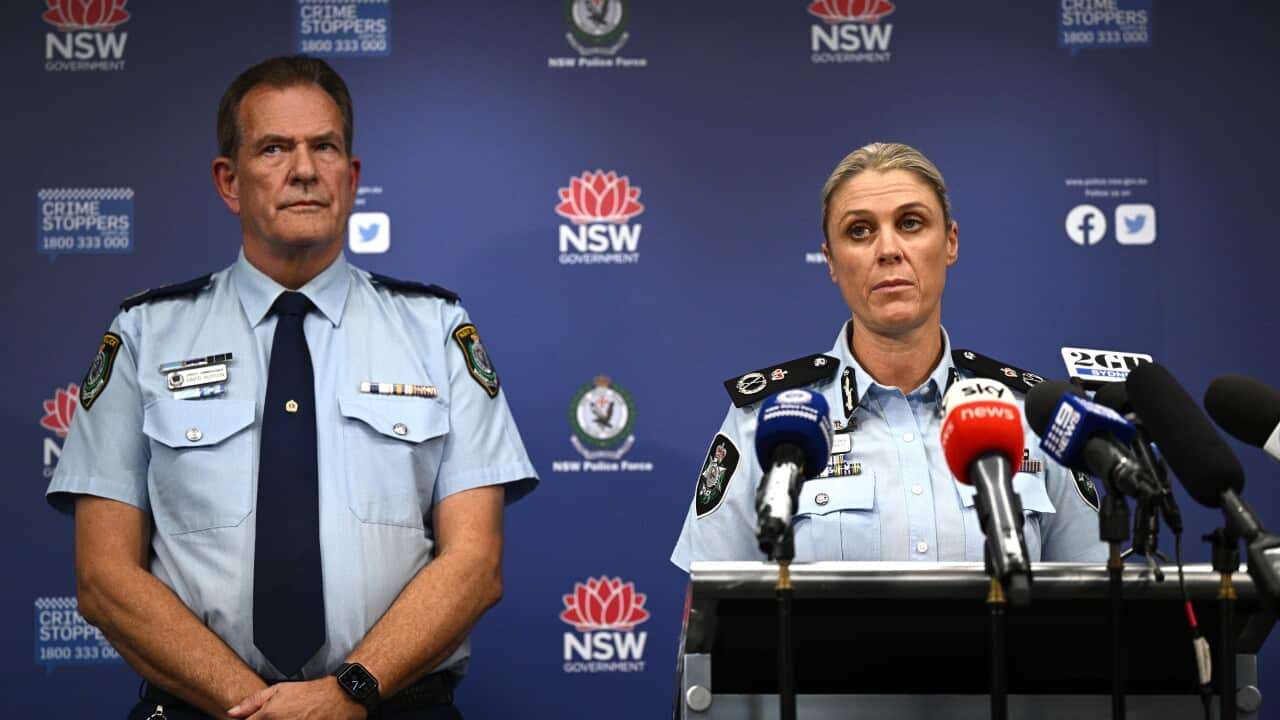 Two police officers stand next to each other in front of a blue banner with NSW Police logos.