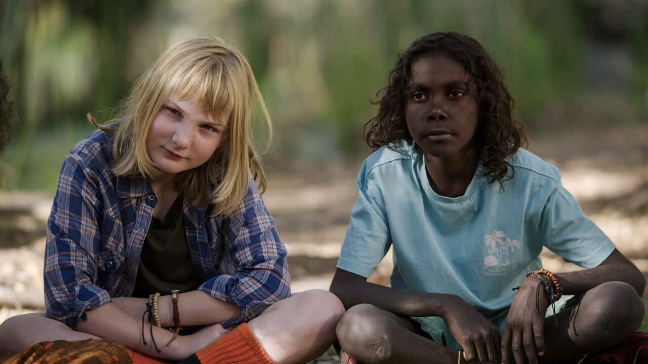 Two young actors; a white girl and an Aboriginal boy, sit next to each other out on Country