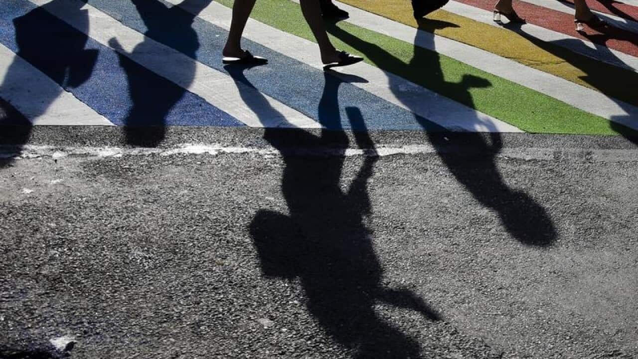 Pedestrians cross a rainbow coloured intersection.
