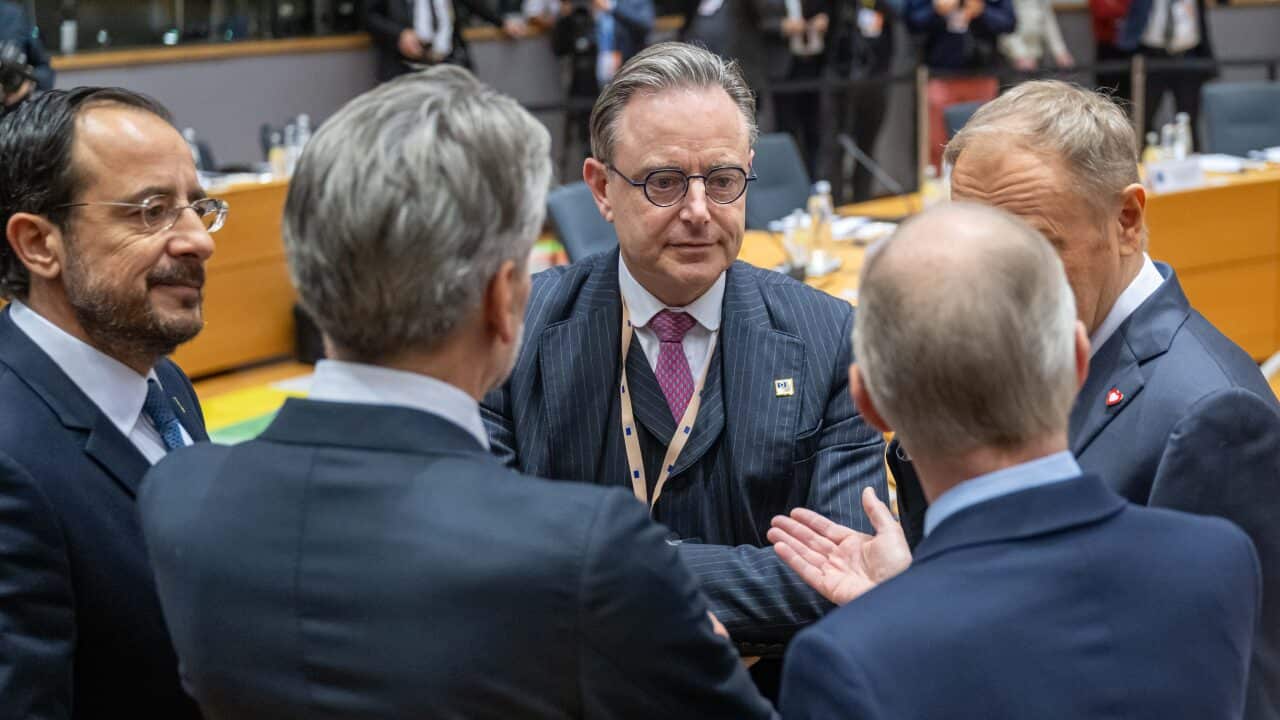 A group of European political leaders wearing suits stand in a circle talking.