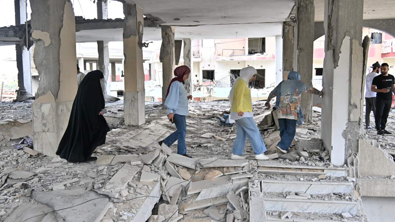 Four women and two men walk through a bombed out building.