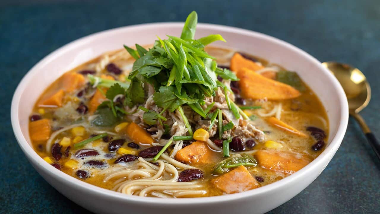 A white bowl holds noodle soup studded with sweet potato and topped with a pile of fresh coriander.
