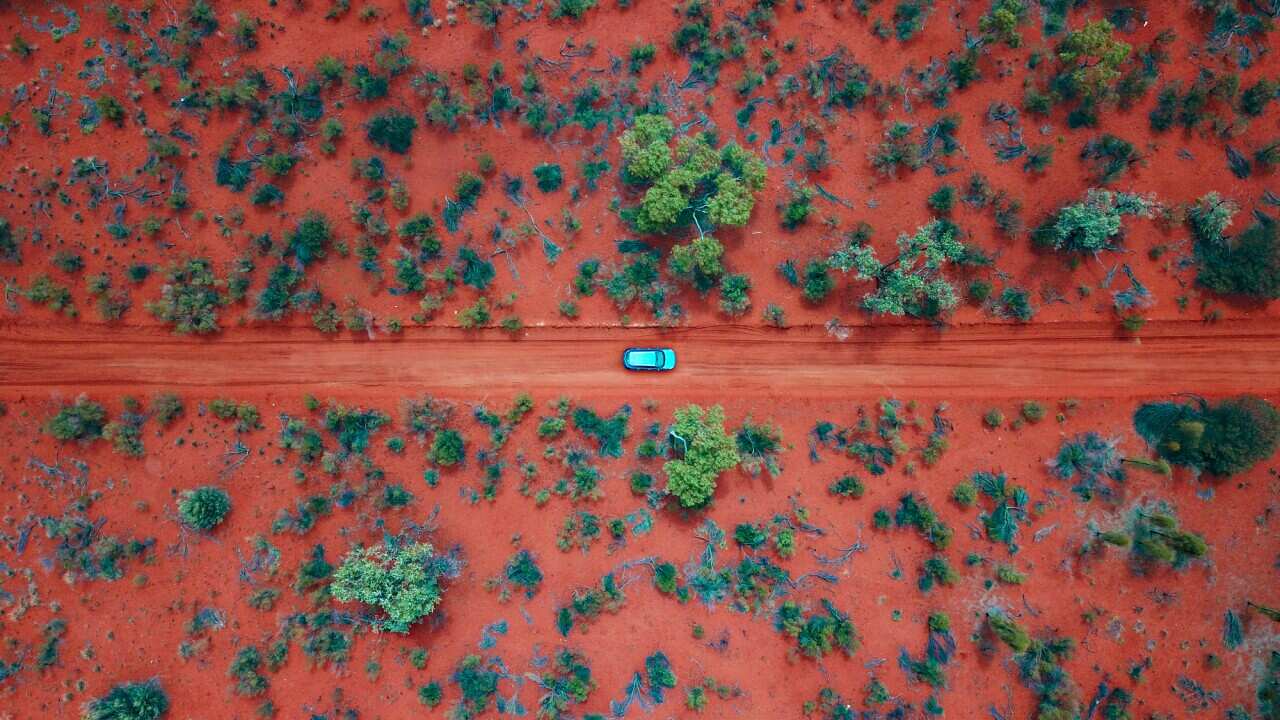 An Aerial shot of a car driving on the red centre roads in the Australian Outback