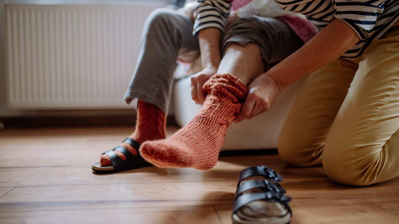 Close-up of healthcare worker putting on warm socks to senior woman.