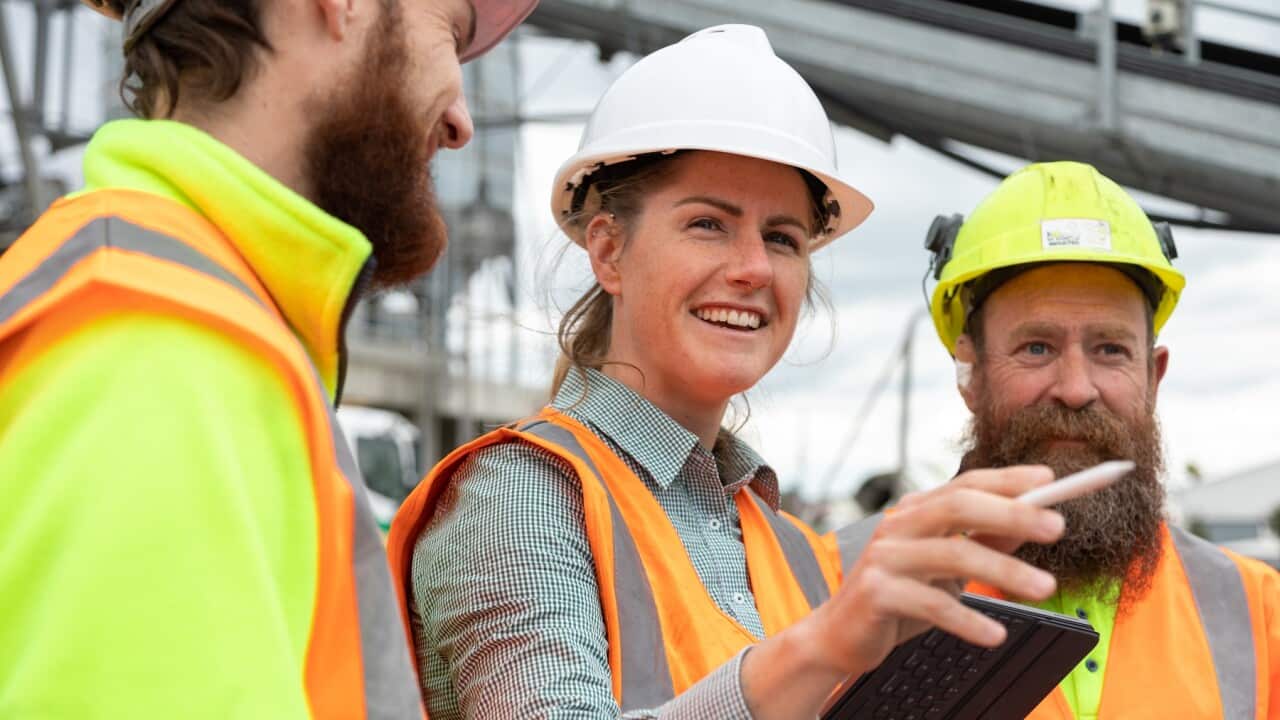 A woman in a leadership role talks to her co workers on a construction /manufacturing site