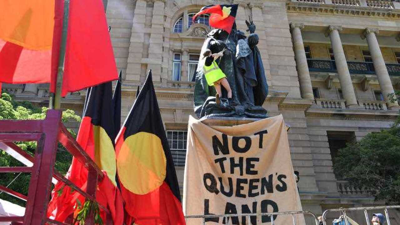 A protestor is seen attaching an aboriginal flag to a statue of Queen Victoria in Queens Gardens during an Invasion Day rally in Brisbane 2021.