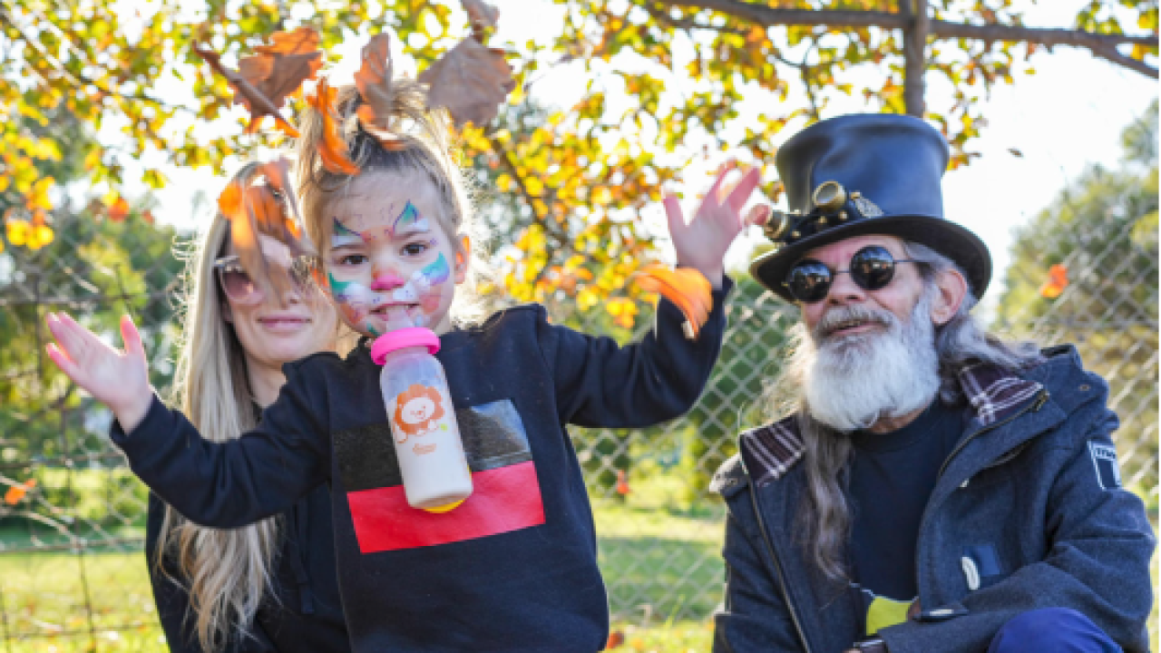 A young child with face paint plays in front of her family outside.