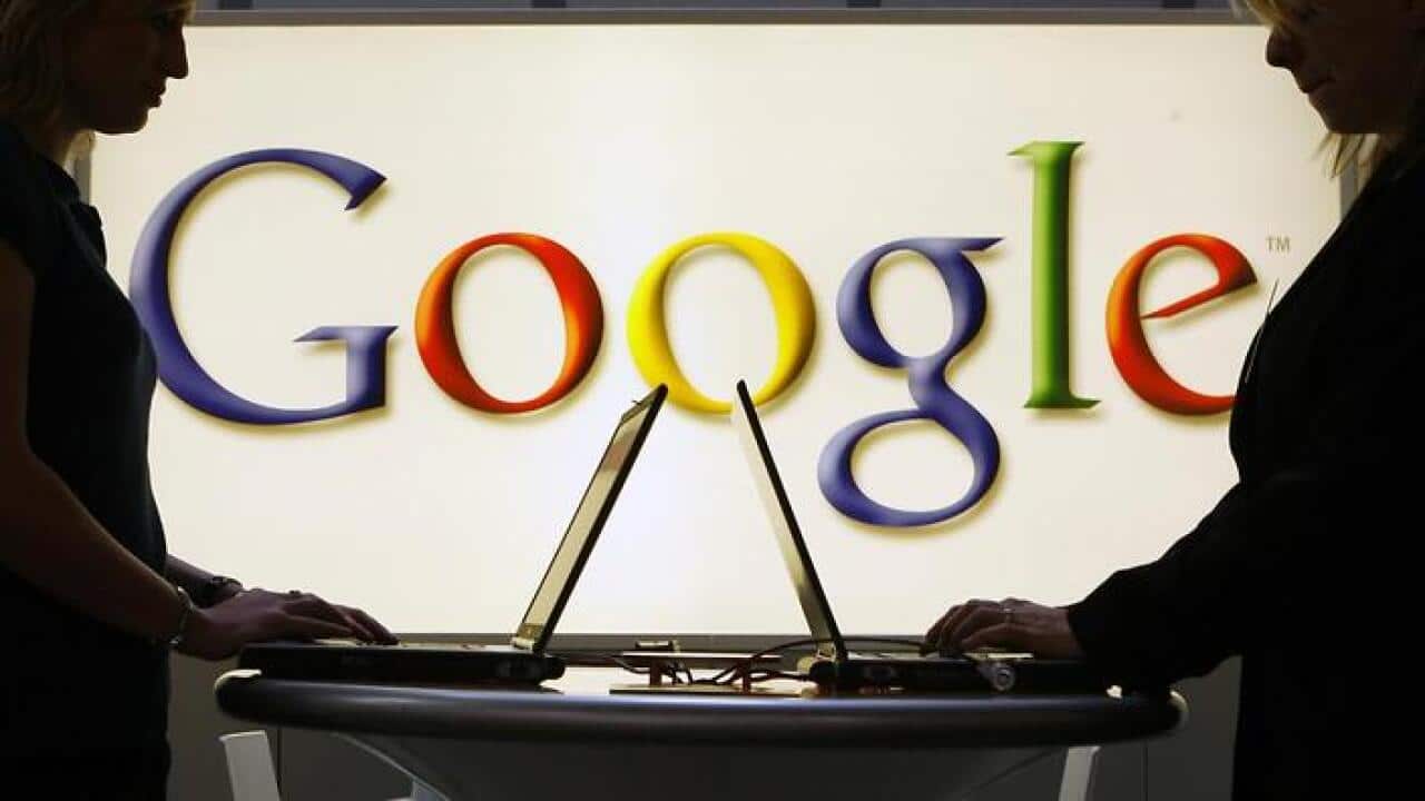 FILE- In this April 17, 2007 file photo, exhibitors of the Google company work on laptop computers in front of an illuminated sign of the Google logo
