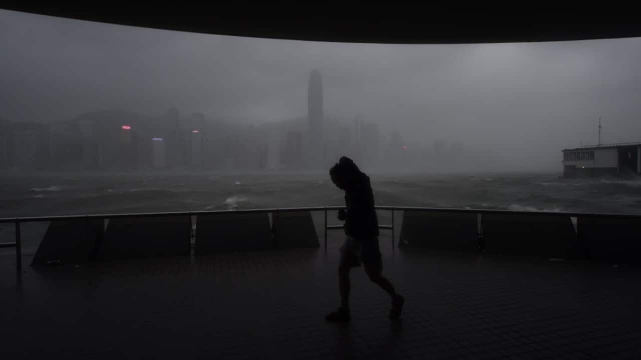 A man tries to walk along the prominade in Tsim Sha Tsui against winds from Typhoon Hato as dark skies hover over the Hong Kong island skyline
