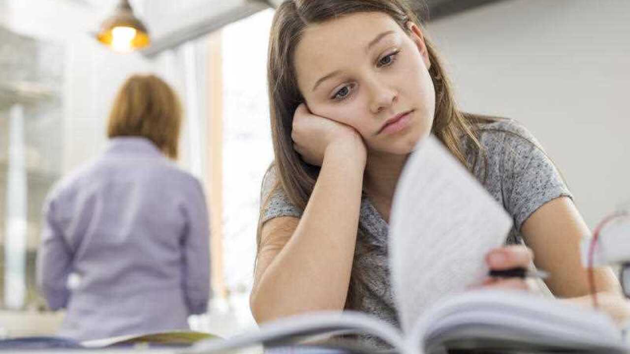 girl studying at table with mother standing in background