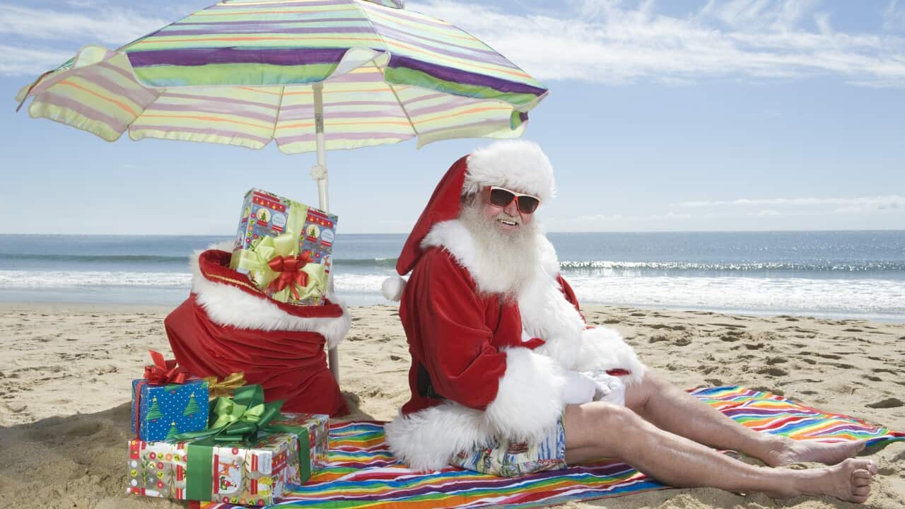 Father Christmas sits under a parasol on the beach. (AAP)