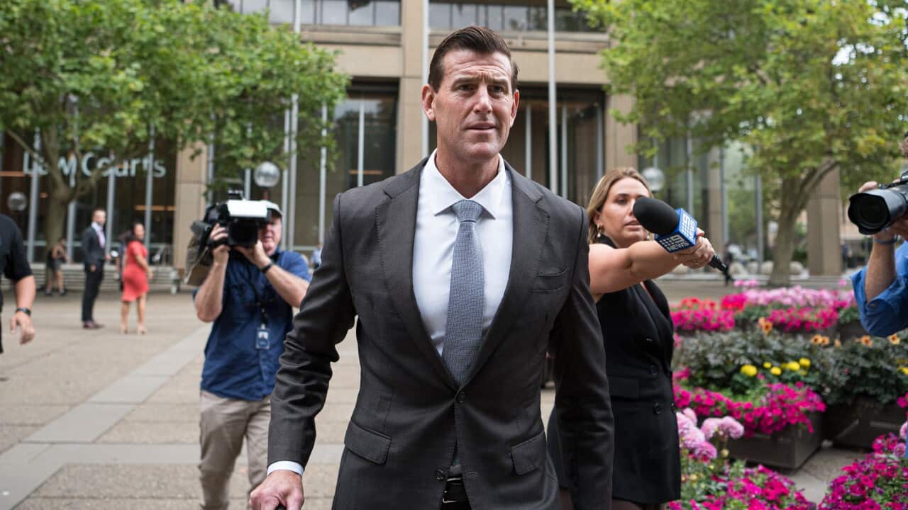 Ben Roberts-Smith walking down a street with journalists and camera operators following him.